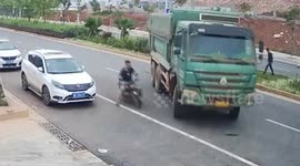 Chinese motorcyclist narrowly avoids serious injuries after falling under truck