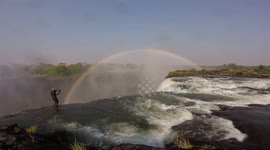 Guy Walks Dangerously Along Edge of Victoria Falls to photograph a beautiful Rainbow