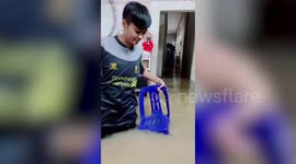 Flood-Hit Resident Sits On Chair To Show Water Depth