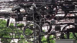 Tangled spider webs of black electricity cables hang over Thai streets