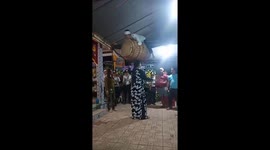 Vietnamese woman balances giant drum with man laying on it on her head