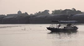A small local ferry carrying one passenger is blocked in mid river and has no choice but to wait, as a large barge passes by in front of him.