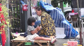 A small kid plays with a smart phone while eating two lollipops and a large cucumber.