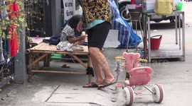 A little kid playing with a smart phone is eating with both hands full, while her grandmother gives her medicine.