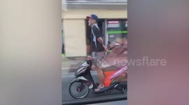 Reckless motorcycle rider stands up without using hands in Thailand