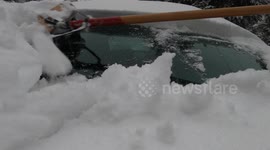 Clearing snow from car windshield with broom after heavy snowfall.