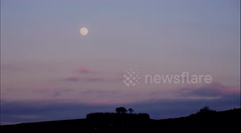Full snow moon rising over ancient Minninglow Tree Henge & Neolithic chambered tomb in the Peak District National Park, Derbyshire, England, UK