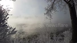 Spectacular winter sunset 4K UltraHD- Between the branches covered by snow and the smoke on the water, you can distinguish the flowing river and the sun.