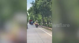 Mother rides motorcycle with food on her head, daughter on the back and bags on front