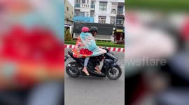 Motorcycle rider and pillion passenger cover themselves with a blanket to keep warm while riding