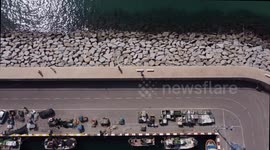 Aerial drone footage from Arenys de Mar Port with people walking and the waves of the sea and the reflection of the sun