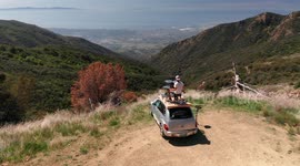 Drummer on top of car plays his drums with a scenic Mountain View