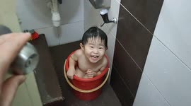 Adorable Malaysian toddler self-bathing in a plastic bucket