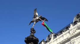 Eros statue with flying flag of Palestine with Free Julian Assange protest underway at Piccadilly Circus