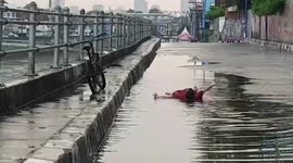 A child playing and lying in a puddle of water on Jalan Raya Jatinegara, East Jakarta, Indonesia