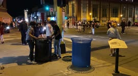 Man struggles to move trash can as protestors attempt to build a blockade in a busy intersection.