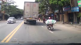 Motorcycle rider carrying big sack clips another rider along road in Vietnam