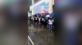 Teachers hold umbrellas over their pupils during downpour in China