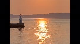 Intense Orange Sunset and Lighthouse on Gentle Ocean Waves During Midnight Sun