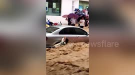 Scooter rider surrounded by rapid floodwater clings onto car before she is rescued in China