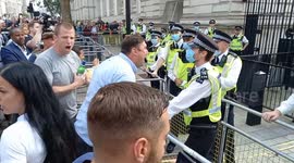 Police officers block angry anti-vaccination protesters from climbing over barricade outside Downing Street