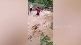 Old man helps dog cross overflowing river after heavy rain in the Philippines