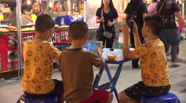 Children play games with smart devices as their parents work in a night market in Thailand.