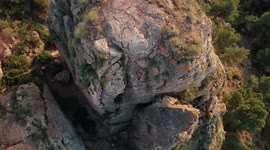 Climbing sportswoman rappelling down the mountain. Drone aerial view of climber woman at mountain top descending it.