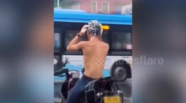 Motorcyclist washes hair with shampoo in the rain when waiting at traffic lights