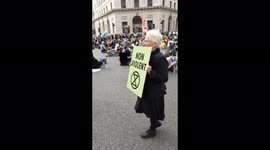 Exstinction rebellion old lady holds a no violence sign. as police look on