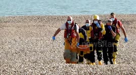 RNLI carry an immigrant on a stretcher up to medics waiting at RNLI hut
