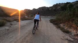 Young girl riding her bike through a dirt road trip over a pothole, and feels down doing a front flip. Afterward, she is attended and helped by the person recording with the camera.