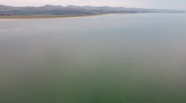 Drone footage panning across Blackrock Sands and Morfa Bychan on the Welsh coast at sunset from the sea