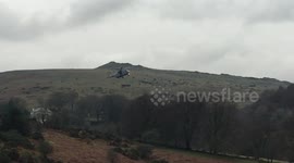 MILITARY HELICOPTER ON A TRAINING EXERCISE IN THE COUNTRYSIDE COMING TO A HOVER LOW ABOVE THE TREES