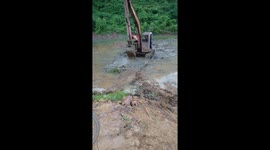 A digger uses its bucket and a metal sheet to cross a muddy swamp in Vietnam