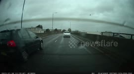 Driver overtakes one car then undertakes another hitting a kerb, makes no progress as traffic is busy on the roundabout, almost hits one car and turns right from the left lane