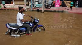 Motorcyclists and pedestrians struggle to pass through submerged streets in southern India