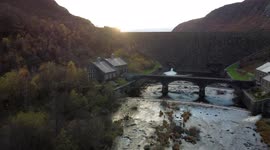 Epic drone flypast up and over the top of a dam in Wales, into the sun setting over the lake, at Elan Valley.