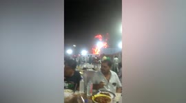 Two wedding guests casually eat dinner while fire rages behind them in India