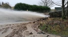 River bursts through Greater Manchester road creating jet of water and stones