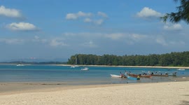An airplain landing in the backgroud of a low tide beach with sail boats and a thai family in the distance