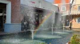 Artificial fountain with reflected bubble water rainbow under clear blue sky