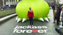 Johnny Knoxville poses for photographers in front of  a giant green phallus-shaped dinosaur in Leicester Square