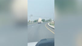 Overloaded truck stacked with hay sways dangerously along road