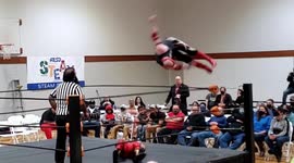Wrestler Spirals off the top rope onto his opponent in a professional wrestling ring