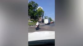 Motorcycle rider carries long steel rods horizontally on road in Thailand