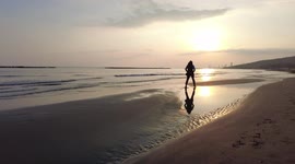 The girl walks along the seashore at sunset. Calm sea, the sun at sunset, the silhouette of a girl against the background of the sea.