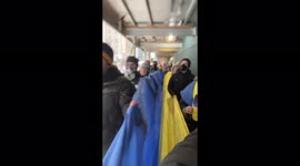 Anti-war protestors march through New York with large Ukrainian flag singing national anthem.