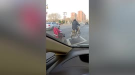 Elderly man cycles along busy road with grandchild in stroller attached to his bike