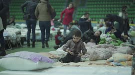 chisinau, moldova - march 4 2022: ukranian refugee boy plays with toy gun at the chisinau arena refugee center with hundres of beds on the background